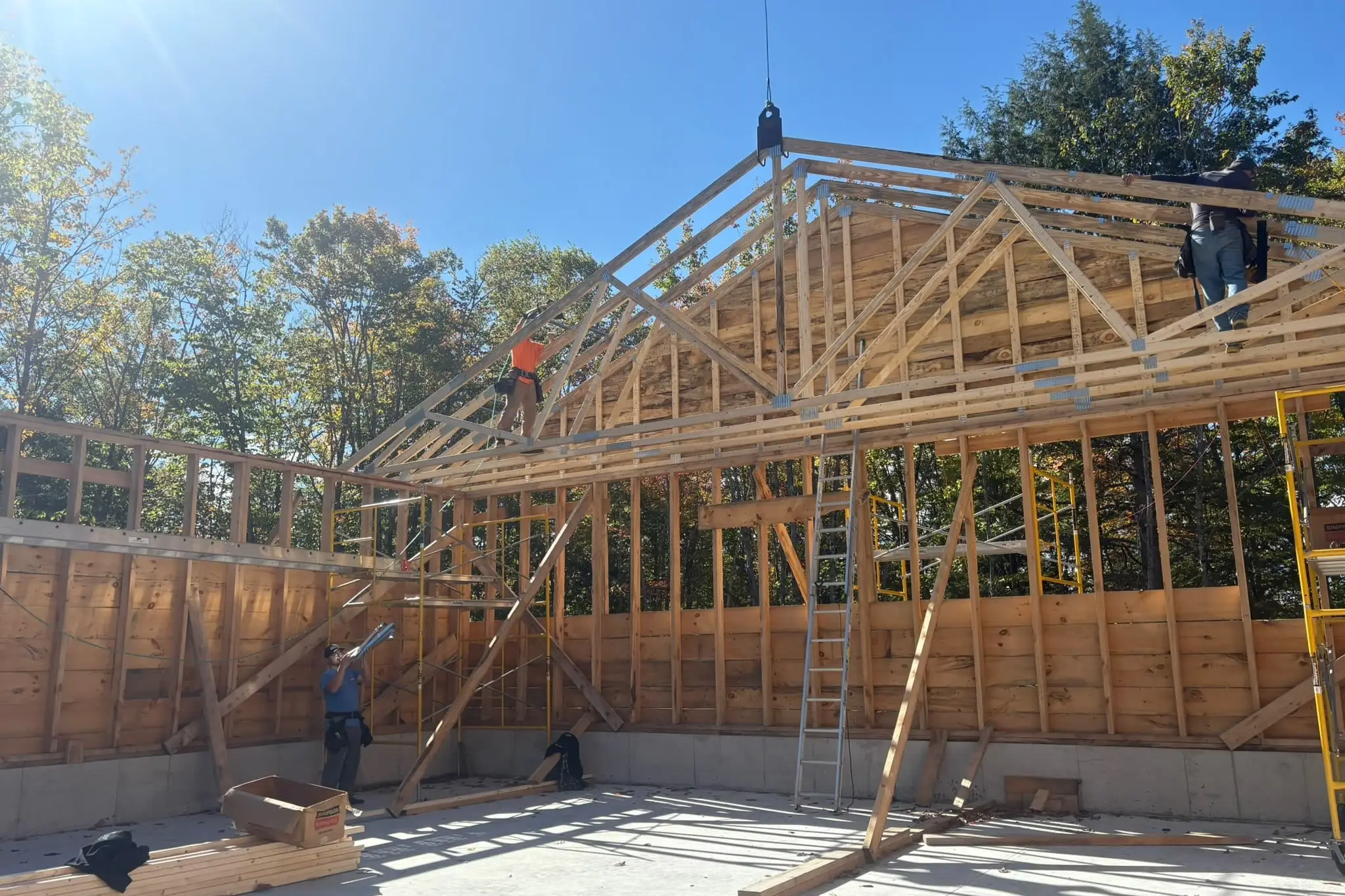 Mariner Construction crew setting a crane-lifted roof truss on a framed building, shot from inside the frame