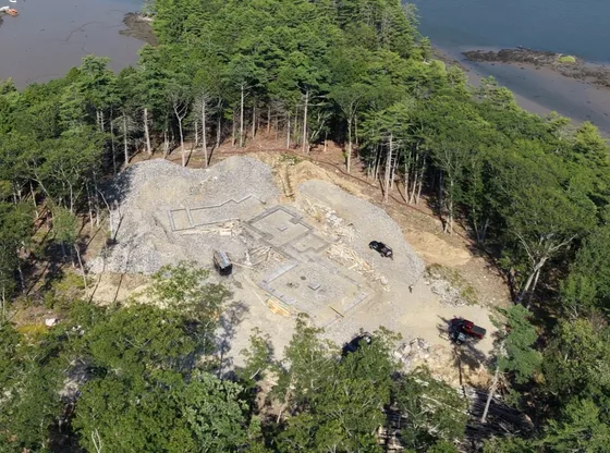 Aerial view of a Mariner Construction house lot: shorefront site cleared and graded, with concrete footings poured