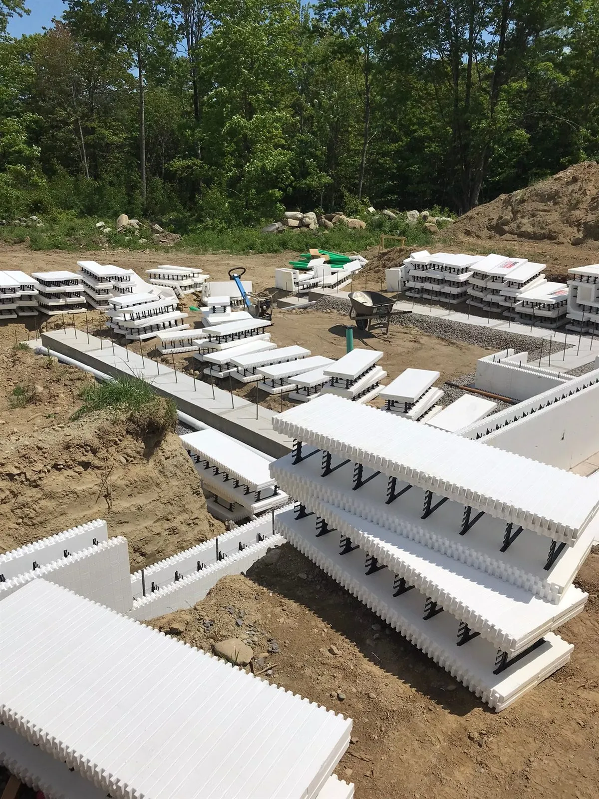 Stacks of white ICF blocks staged around freshly poured concrete footings