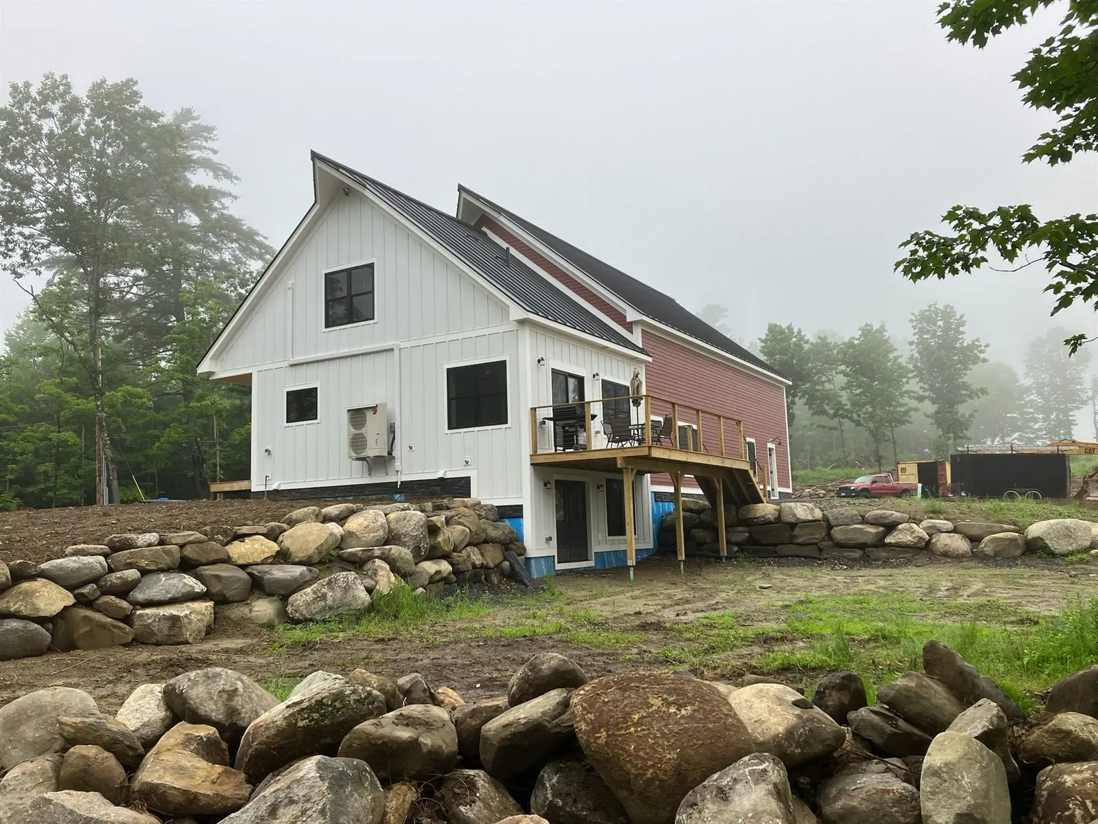 The finished house in morning fog: white board-and-batten gable, red siding, and a deck