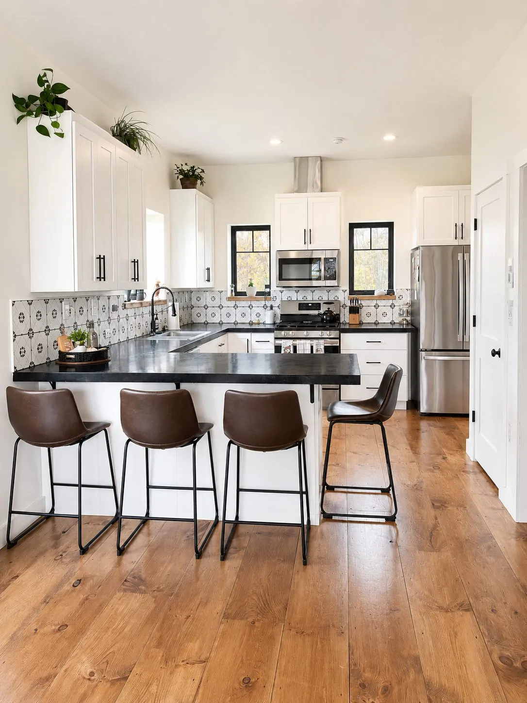 The finished kitchen: white cabinets, dark countertops, patterned tile backsplash, and wide pine floors