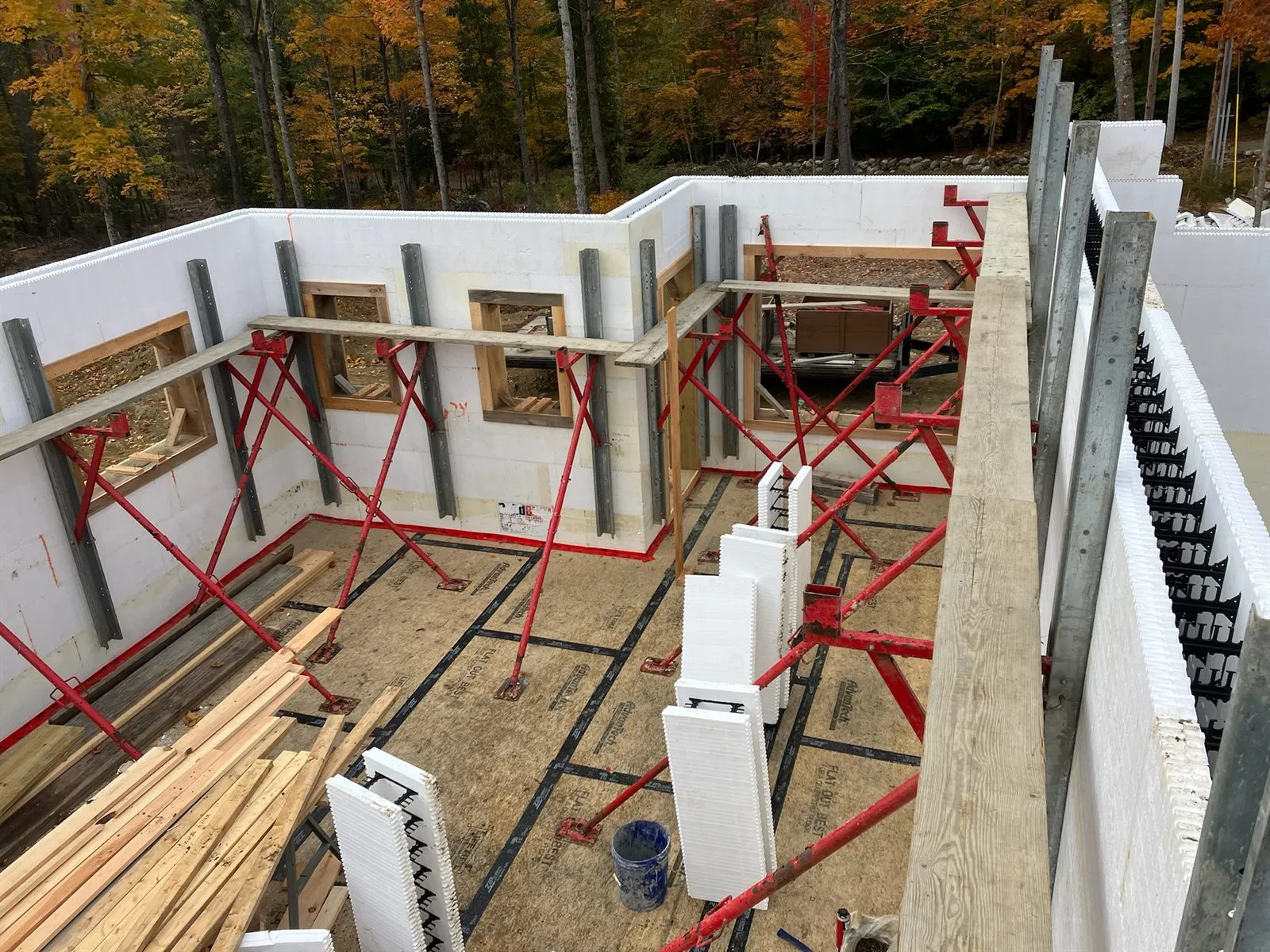 Second-floor ICF walls braced, window openings bucked, fall woods behind