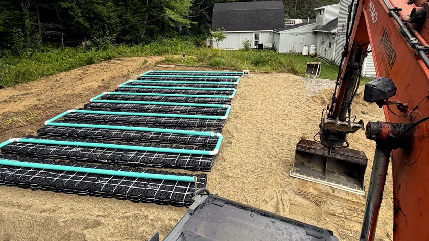 Rows of septic chambers in a fresh sand bed, seen from the cab of a Mariner Construction excavator